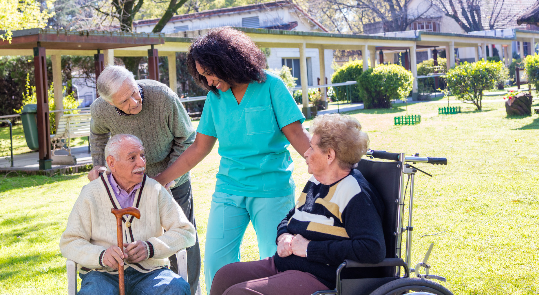 Afroamerican nurse joking with elder disabled people outdoor.